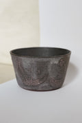 Dark ceramic pot on a light surface with a neutral background