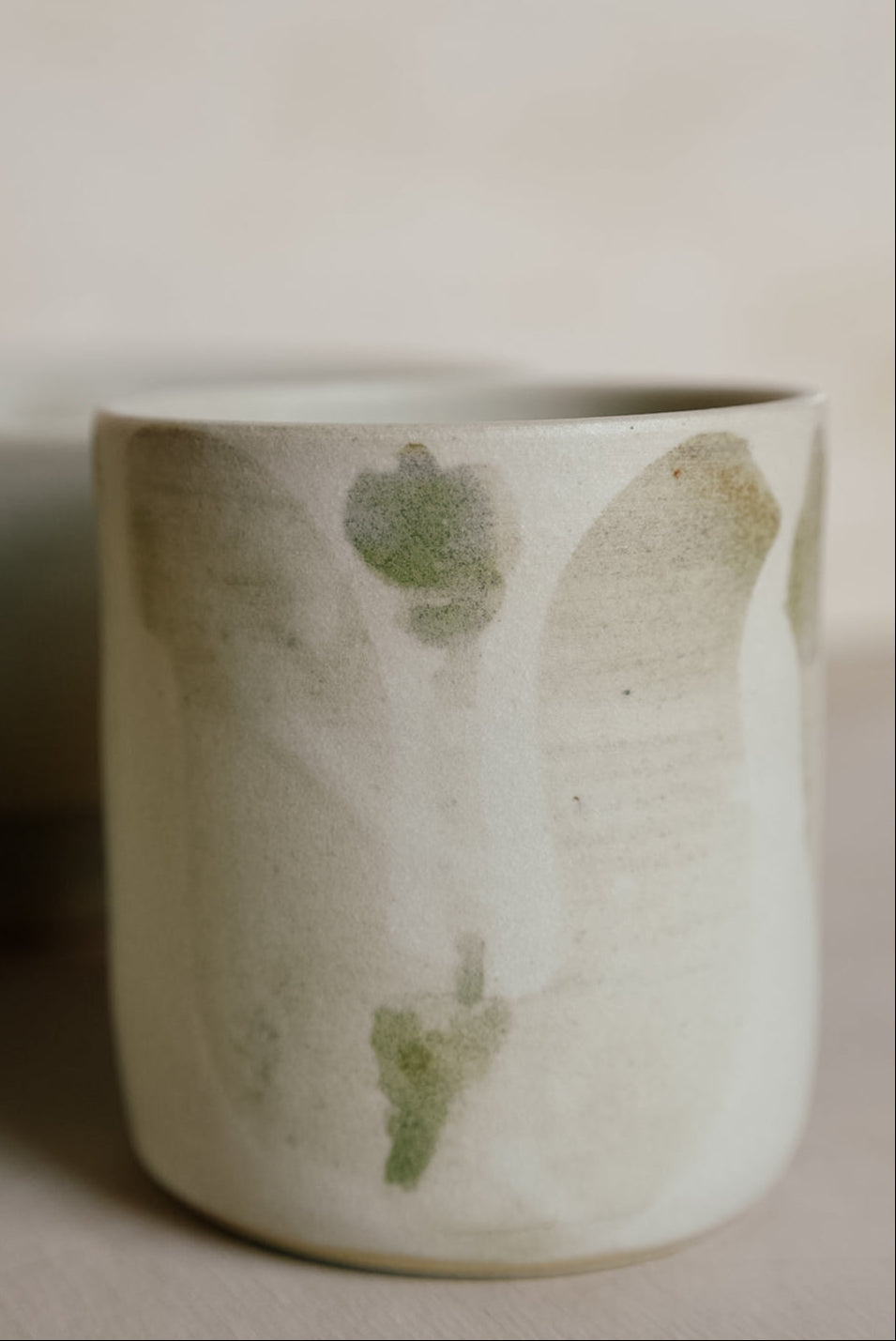 White ceramic cup with greenish-brown speckles and a tulip drawing on a neutral background