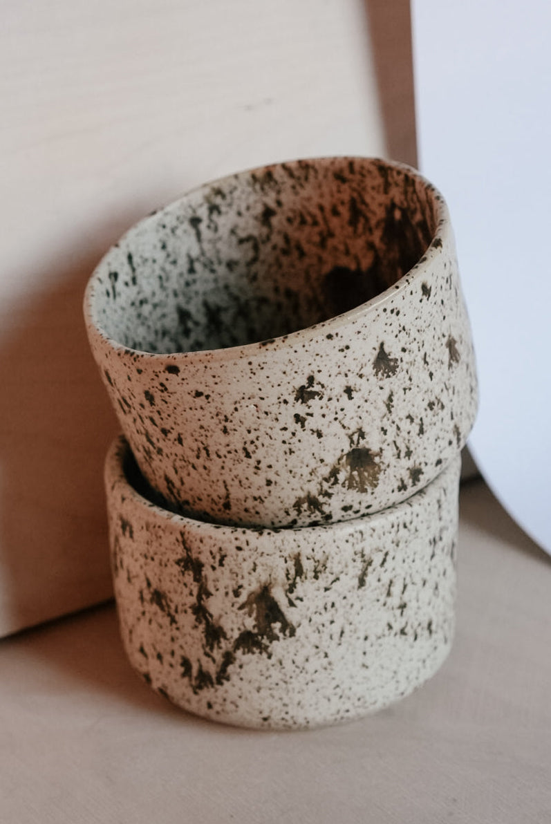 Two stacked ceramic cups with speckled texture on a neutral background