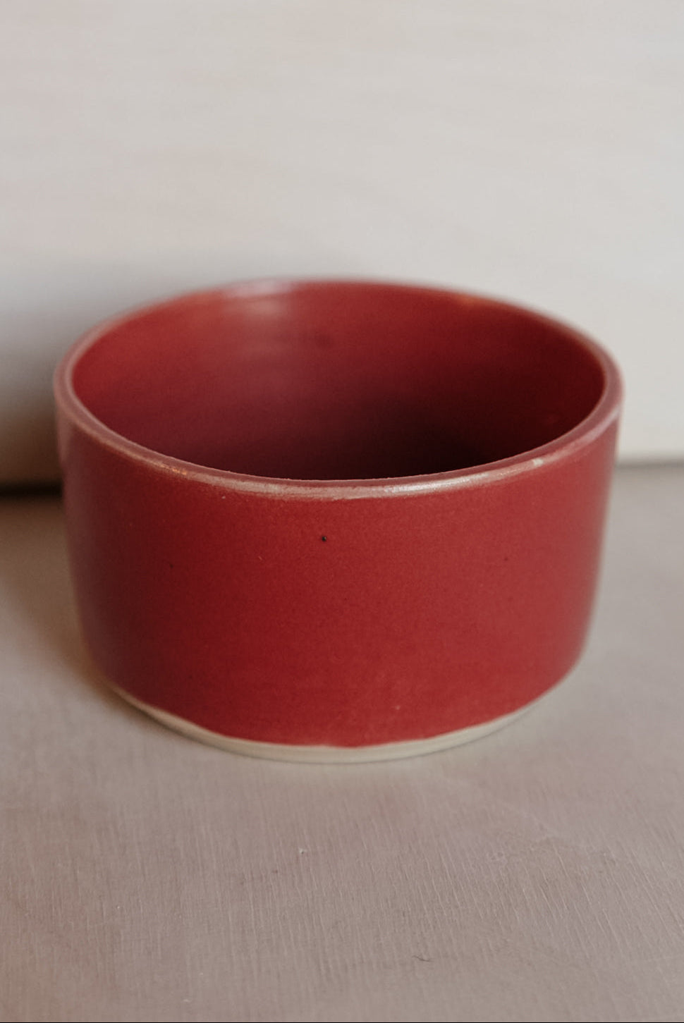 Red ceramic cup on a beige surface with a white background