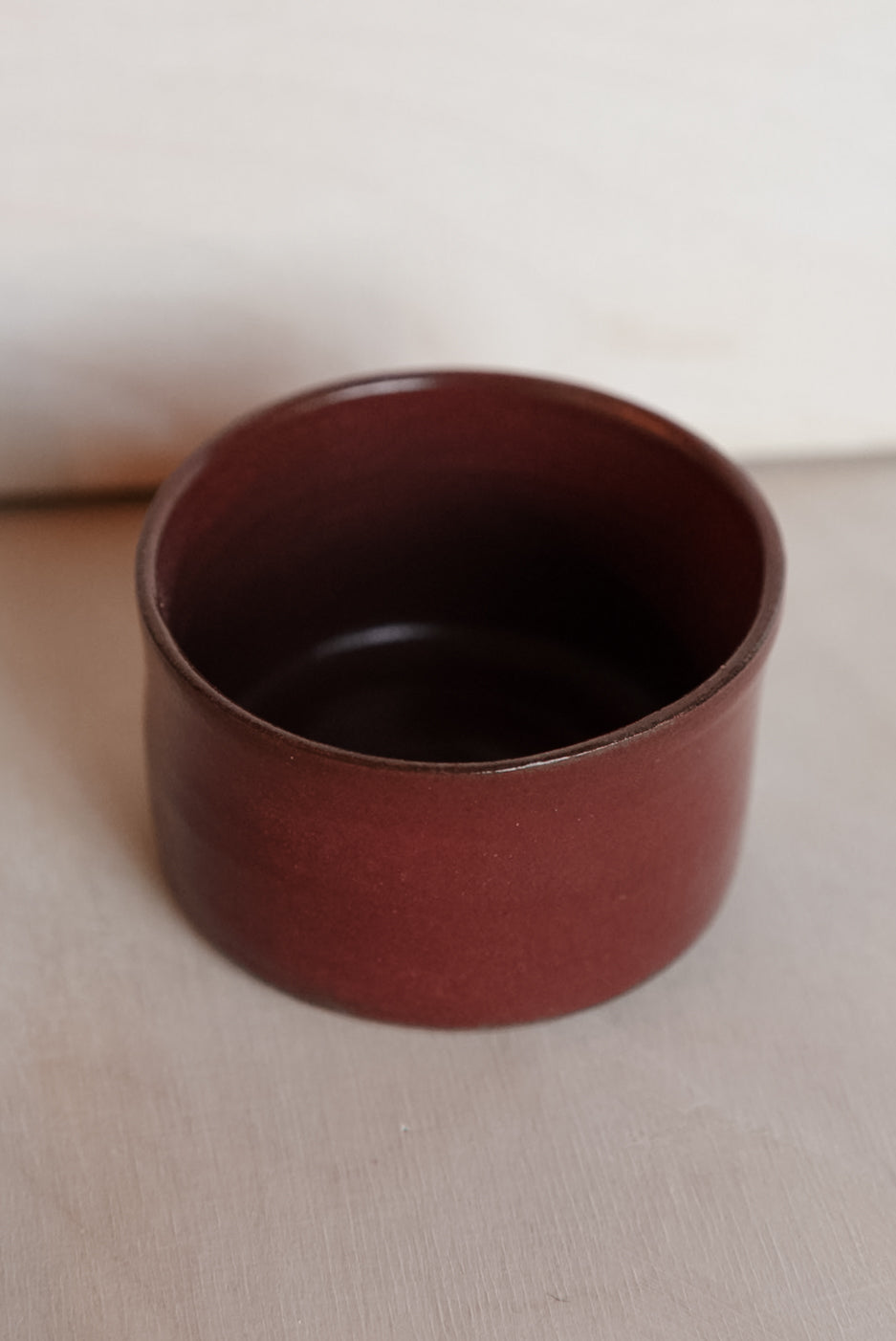 Dark red ceramic cup on a beige surface with a white background