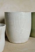 A handmade ceramic vase with a white crackle glaze and subtle branch-like raised patterns, displayed on a light wood surface.