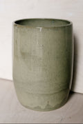 A ceramic vase in a muted sage green glaze, shown against a neutral off-white background.