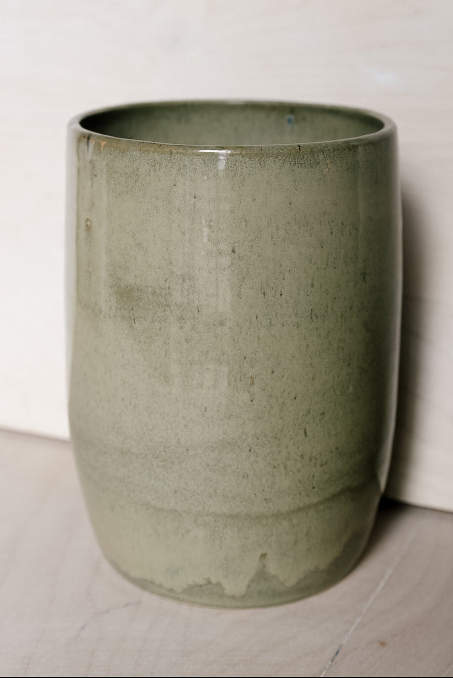 A ceramic vase in a muted sage green glaze, shown against a neutral off-white background.