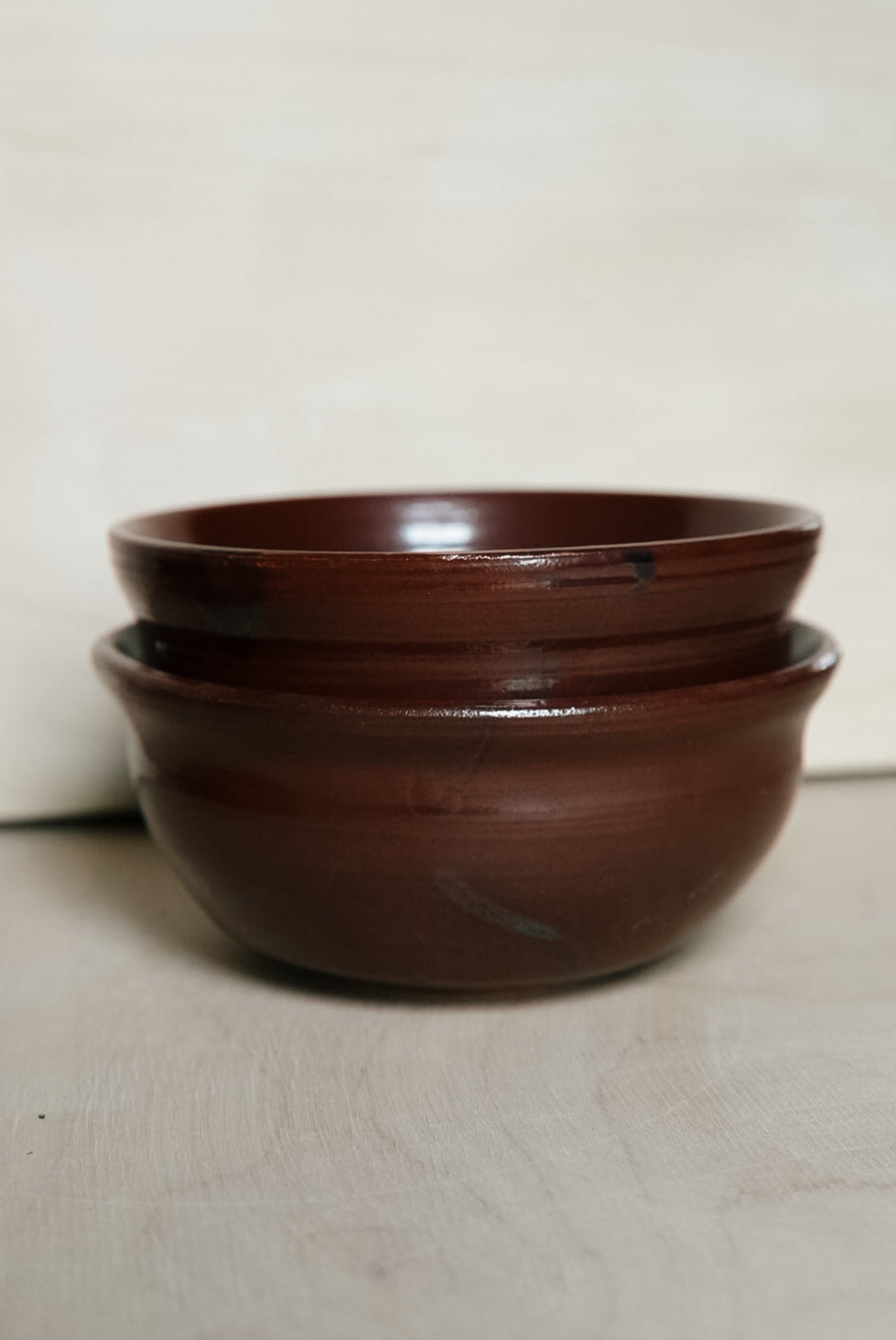 Two stacked dark red ceramic bowls with a glossy finish, set against a light beige background.