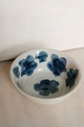 A small white ceramic bowl decorated with hand-painted dark blue floral motifs, resting on a light wood surface.
